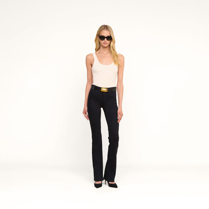 A woman with long blonde hair wearing sunglasses, the Nica Scoopneck Bodysuit in beige, black belted pants, and black heels stands against a plain white background.