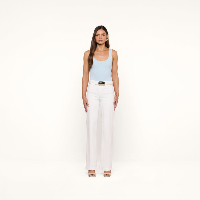 A woman stands facing forward against a plain white background, wearing a light blue Nica Scoopneck Bodysuit with a sculpted fit, paired with white high-waisted pants featuring a belt and open-toed heels.