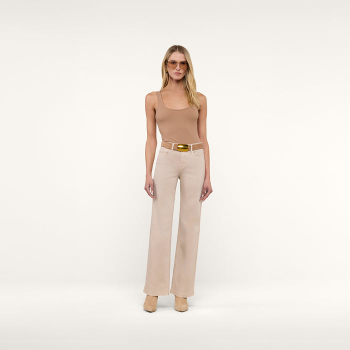 A woman stands facing forward against a plain white background, wearing sunglasses, the Nica Scoopneck Bodysuit in sleeveless camel stretch rib, beige wide-leg pants with a belt, and tan shoes.