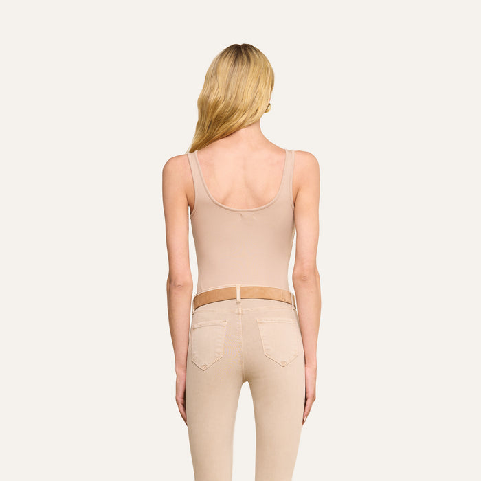 A person with long blonde hair is shown from the back, wearing the Nica Scoopneck Bodysuit in beige along with light beige jeans and a tan belt, standing against a plain light background.