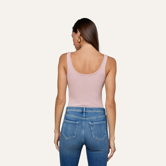 A woman is shown from the back, wearing the Nica Scoopneck Bodysuit in light pink, paired with blue jeans featuring visible back pockets, against a plain light background.
