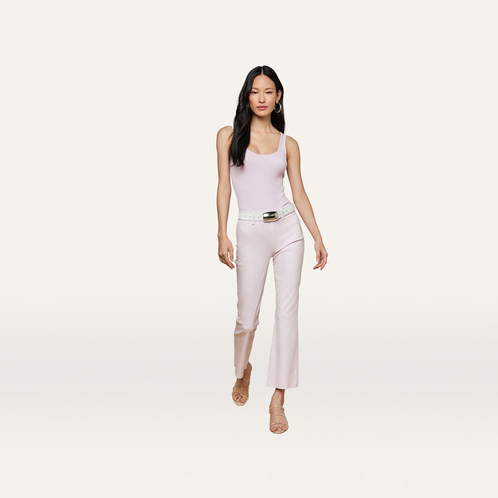 A woman walks forward against a plain light background wearing the Nica Scoopneck Bodysuit in light pink, matching pants, a white belt, and beige sandals.