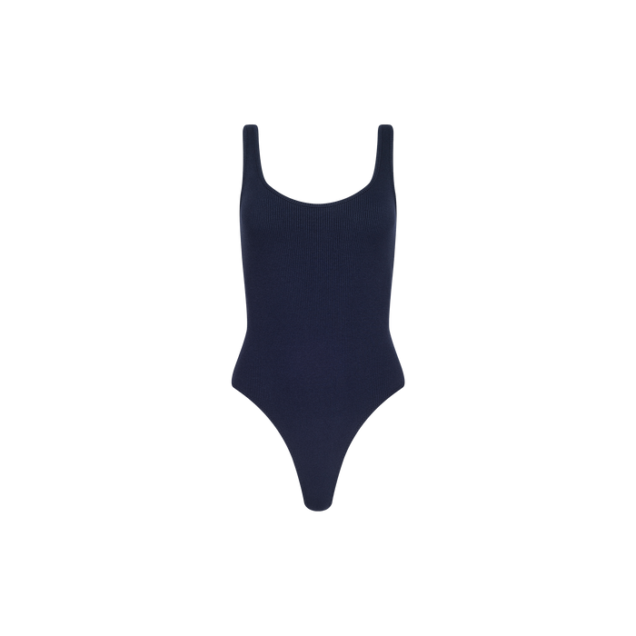 The Nica Scoopneck Bodysuit is a sleeveless, navy blue ribbed piece with a sculpted fit, featuring a scoop neckline and high-cut legs, shown against a plain white background.