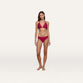 Woman standing barefoot on a plain white background, confidently showcasing the Nicole Bikini Bottom—a matching red bikini with scalloped edges and halter neck top in a rich black cherry hue, making it a true swim essential. She looks at the camera with arms relaxed by her sides.