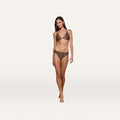 A woman stands against a plain white background, facing forward with a relaxed expression and one leg slightly in front of the other, wearing the Nicole Bikini Bottom in leopard print made from four-way stretch nylon.