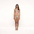 A woman stands facing forward, wearing the Nicole Bikini Bottom featuring a colorful abstract swirl print crafted from stretch nylon with UPF 50 protection, set against a plain white background.