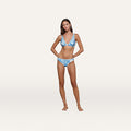 A woman stands with hands on her hips, wearing the Nicole Bikini Bottom—a blue and white floral bikini crafted from four-way stretch nylon for comfort and moderate coverage—set against a plain light background.