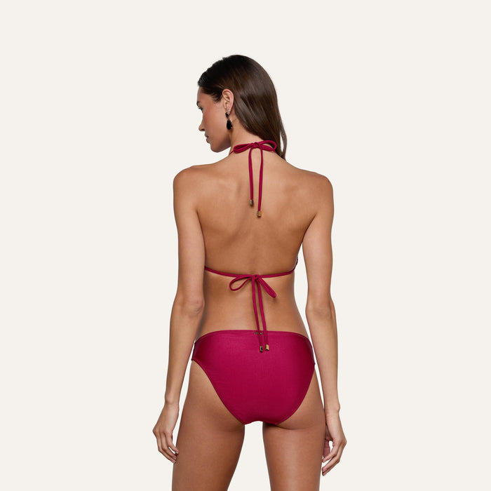 A woman with long brown hair is seen from behind, wearing a magenta halter and tie-back bikini top paired with the Nicole Bikini Bottom, standing against a plain, light background.