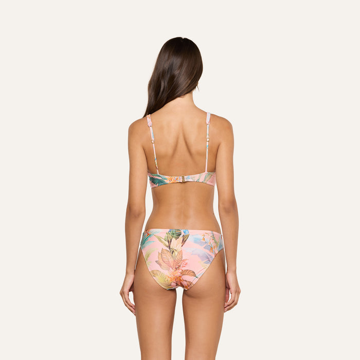 Woman with long brown hair, seen from behind, wearing the Nicole Bikini Bottom in a pink floral print made from stretch nylon, against a plain light background.