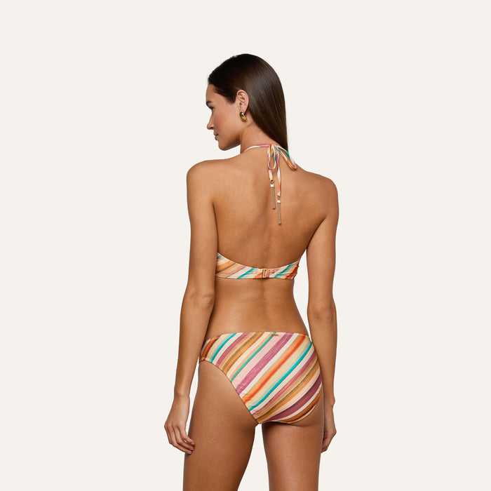 A woman with long brown hair models the Nicole Bikini Bottom, a moderate coverage swimsuit featuring a retro watercolor stripe, shown from the back against a plain light background.
