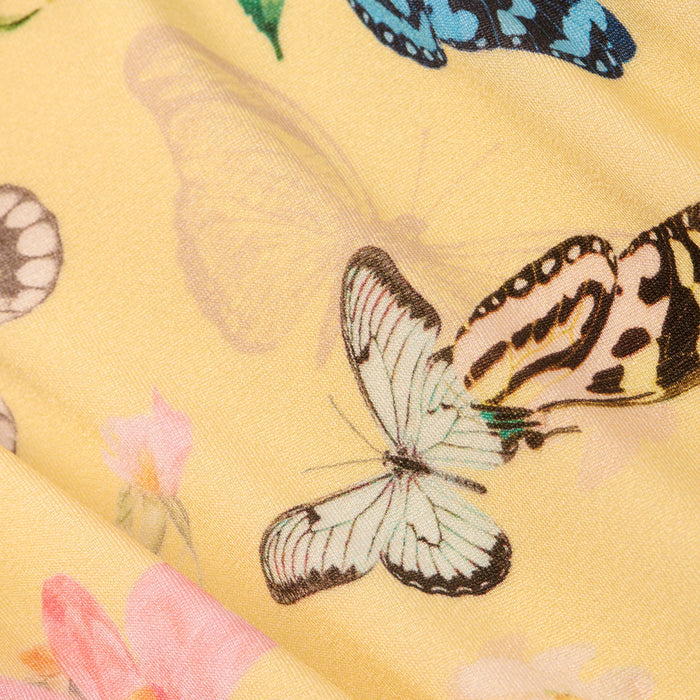 Close-up of the Nicole Bikini Bottom’s yellow fabric, showcasing a delicate and vibrant pattern with multicolored butterfly prints—featuring blue and white—and pink flowers.