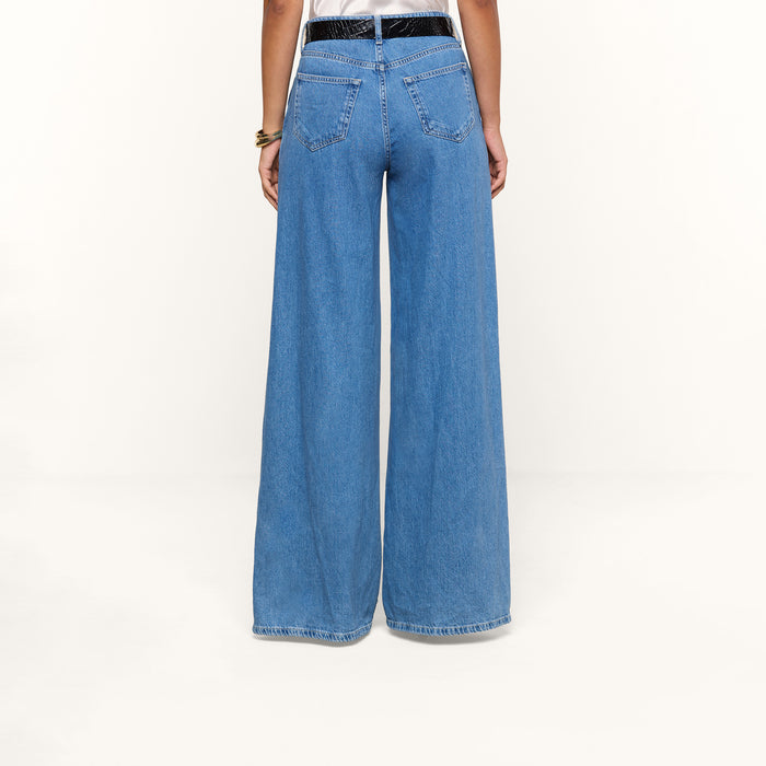 A person wearing the Niles Wide-Leg Jean in light blue—a high-rise, wide-leg style crafted from lightweight denim—and a white top, shown from the back against a plain white background.