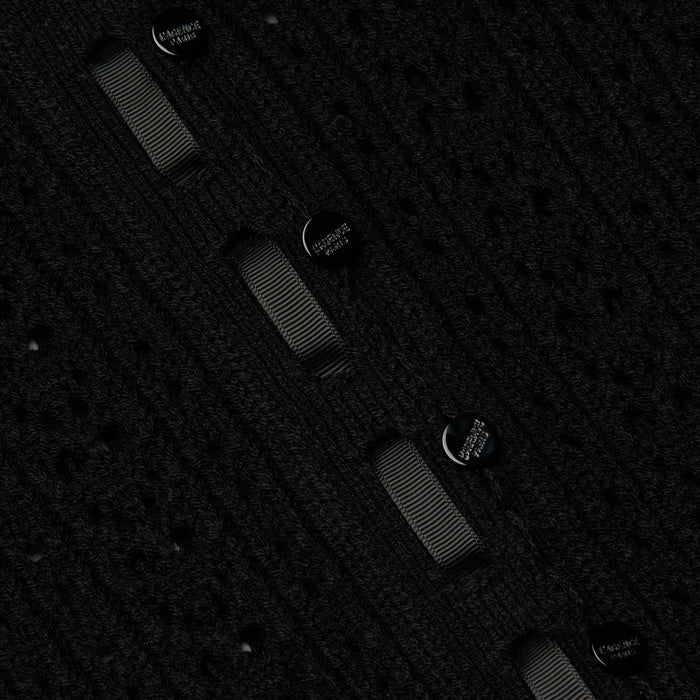 Close-up of the Ninette Knit Top in black, featuring a textured fabric with eyelet patterns, grosgrain ribbon trim woven through, and metallic buttons detailed with delicate engraved text for a hint of Parisian charm.