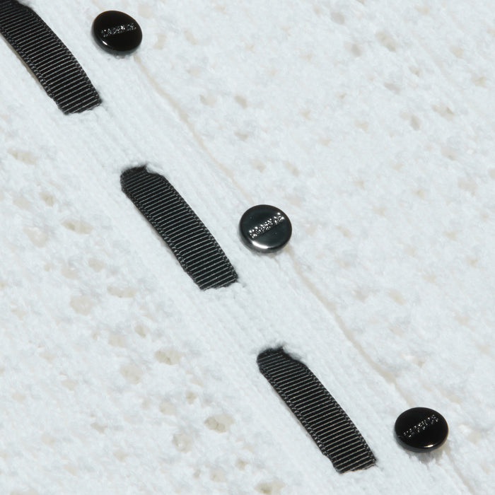 Close-up of the Ninette Knit Top, featuring textured white fabric, three black round buttons, and parallel grosgrain ribbon trims stitched vertically for a touch of Parisian flair.