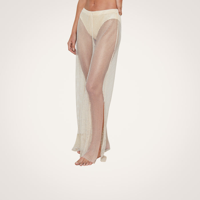 A person is wearing the Noemi Mesh Cover-Up Pant in champagne with a flared leg over beige underwear, standing barefoot against a plain white background.