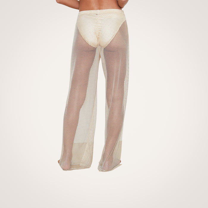 A person is shown from the back against a plain, light background, wearing the Noemi Mesh Cover-Up Pant over a bathing suit bottom.