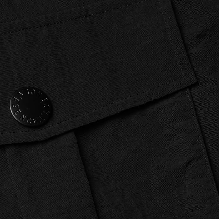 Close-up of the Norene Nylon Mini Skirt in black, showcasing its textured water-repellent nylon fabric, a flap detail, and a black button engraved with text. The visible stitching highlights the garment’s quality construction.