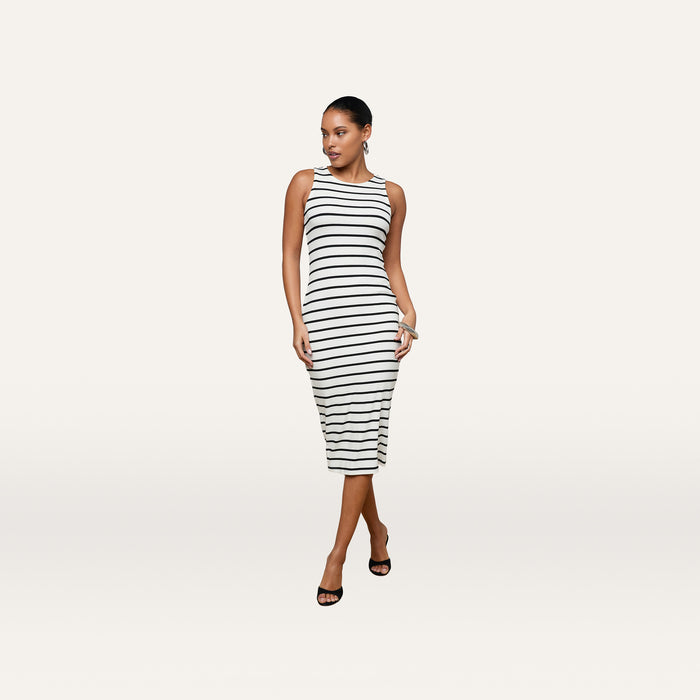 A woman stands against a plain white background wearing the Nura Racerback Midi Dress—a sleeveless, black and white striped jersey day dress with a racerback silhouette—paired with black heels.