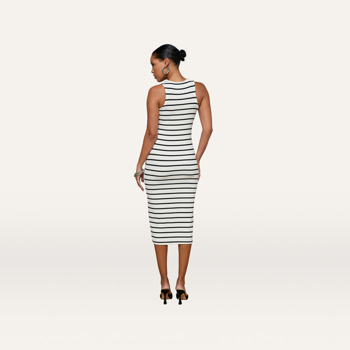 A woman wearing the Nura Racerback Midi Dress, a black-and-white striped, sleeveless, fitted midi dress with a racerback silhouette, stands facing away in black heels, her hair styled in a bun.