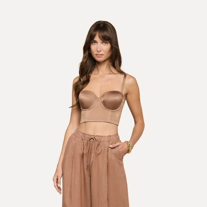 Woman with long brown hair wearing the Nysa Bustier Top in tan, paired with high-waisted drawstring pants, standing against a plain light background with her left hand in her pocket.