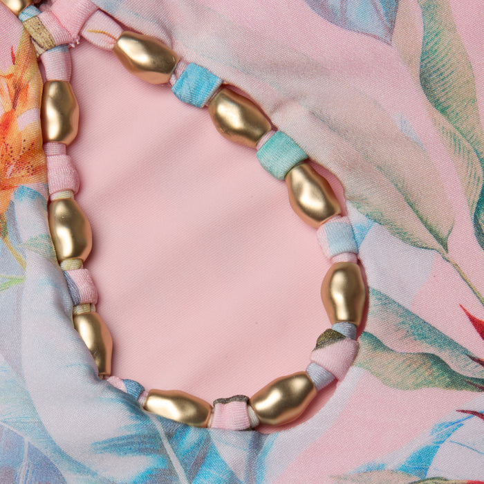 Close-up of the Opus Halter One-Piece Swimsuit in pink floral fabric, featuring a loop of gold oval beads threaded on multicolored fabric strips.
