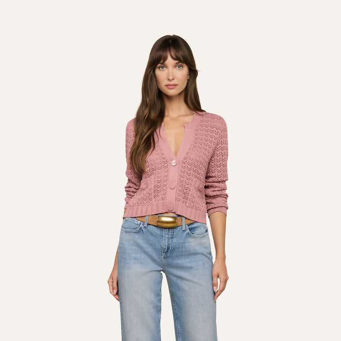 A woman with long brown hair is wearing the Orla Pointelle Knit Cardigan in mauve and light blue jeans, standing against a plain off-white background and looking at the camera with a neutral expression.