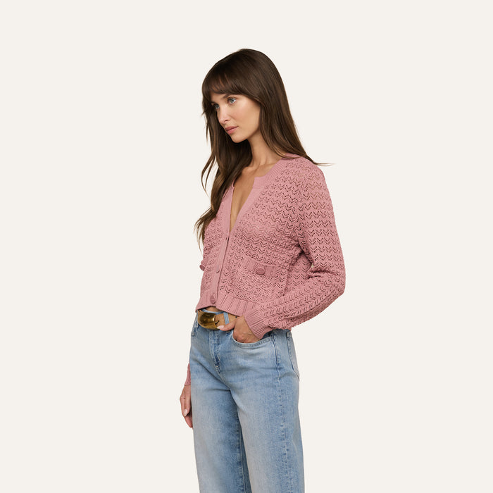 Woman with long brown hair wearing the Orla Pointelle Knit Cardigan in mauve and light blue jeans, standing and looking to the left against a plain off-white background.