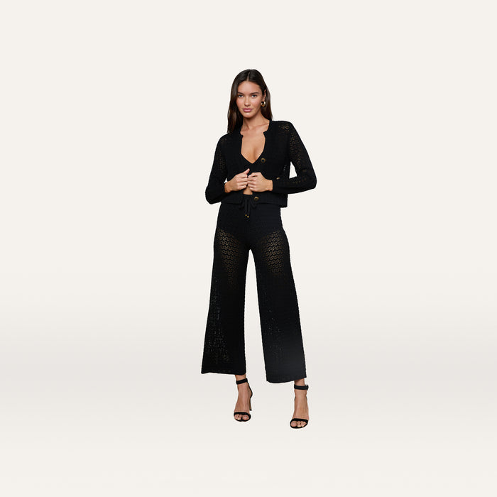 A woman stands against a plain light background wearing the Orla Pointelle Knit Cardigan paired with matching wide-leg pants and black high-heeled sandals.