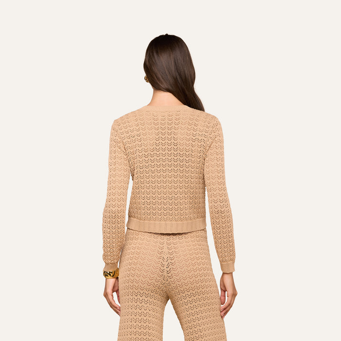 Woman with long brown hair, wearing the Orla Pointelle Knit Cardigan in beige as part of a matching set, facing away from the camera against a plain light background.