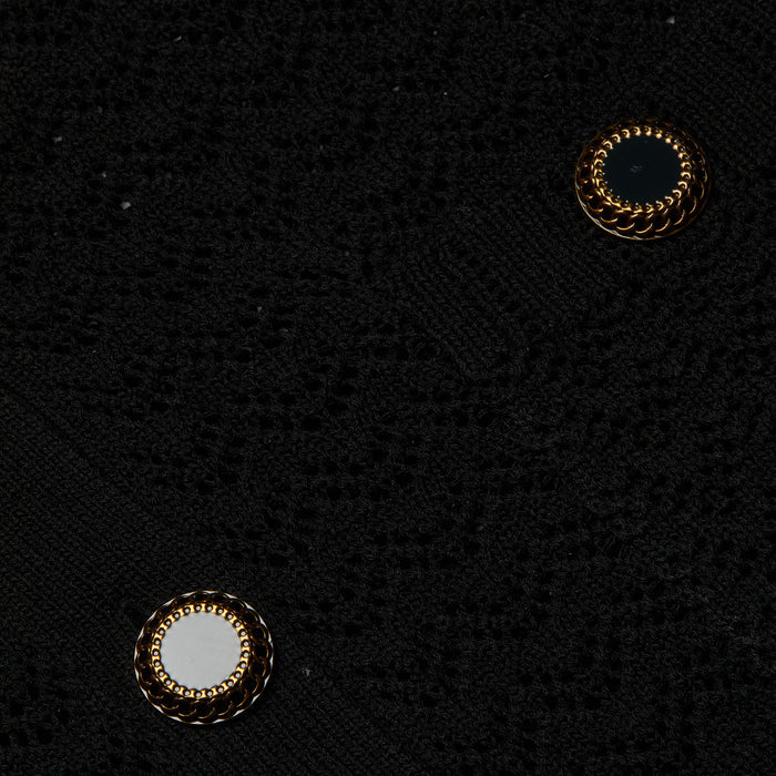 Close-up of the Orla Pointelle Knit Cardigan in black, showcasing its pointelle knit fabric and two decorative buttons—one black and one white—each outlined with a gold braided design, accentuating the detailed craftsmanship of this lightweight beach cover-up.
