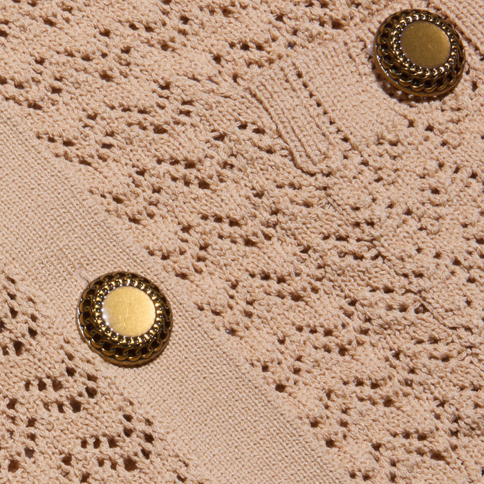 Close-up of the Orla Pointelle Knit Cardigan, featuring textured beige fabric with an intricate lace-like pointelle knit pattern and two round gold buttons with decorative edges.