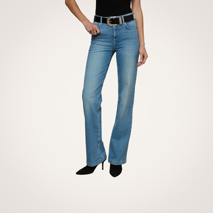 A woman models light blue straight-leg jeans, the Otera Leather Belt featuring a croc-embossed finish with a floral engraved buckle, and black high-heeled shoes against a plain background. Her head is not visible.