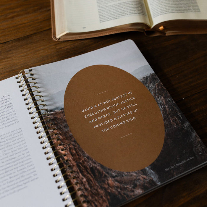 Peaks and Valleys Mens Spiral Study opened to a short devotional page up close on a brown wooden table next to an open book
