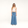 A person wearing sunglasses, a beige sleeveless top, the Petite Quincy Wide-Leg Jean in blue with a brown belt and brown shoes stands against a plain white background.