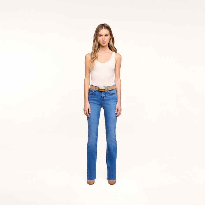 A woman stands against a plain white background wearing a white tank top, brown belt, brown shoes, and Petite Ruth Straight-Leg Jean in heritage indigo wash.