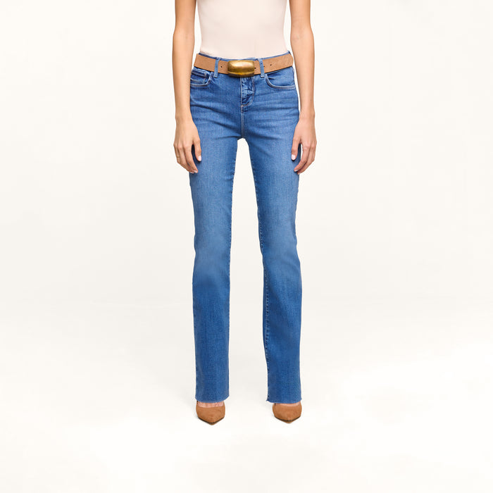 A person is shown from the shoulders down, wearing a sleeveless beige top, a brown belt, brown pointed-toe shoes, and heritage indigo wash Petite Ruth Straight-Leg Jean, standing against a plain white background.