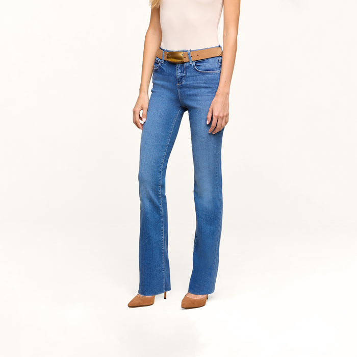 A woman wearing Petite Ruth Straight-Leg Jeans in heritage indigo wash, a tan belt, a sleeveless beige top, and tan high-heeled shoes stands against a plain white background.