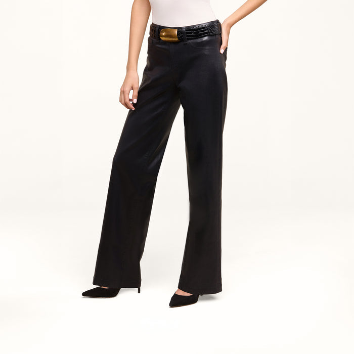 A person wearing the Petite Scottie Coated Jean, styled with a white top, a black textured belt featuring a gold buckle, and black pointed-toe heels stands against a plain white background.