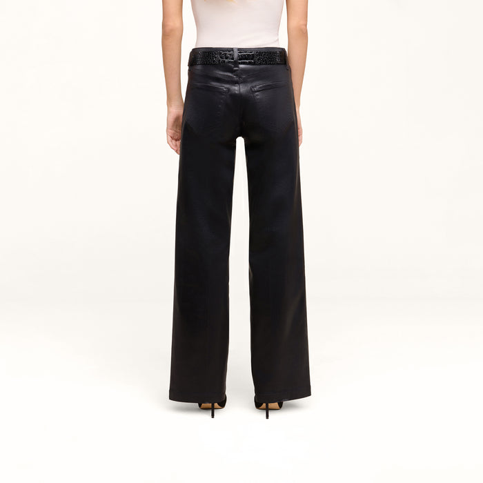 A person is shown from the back against a plain white background, wearing the Petite Scottie Coated Jean, styled with a black belt and black high-heeled shoes.