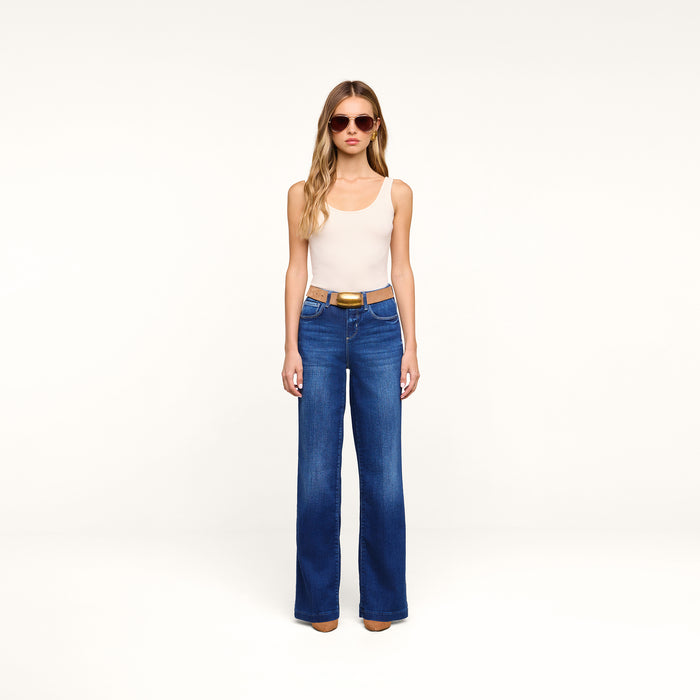 A woman models the Petite Scottie Wide-Leg Jean, paired with sunglasses and a cream tank top, standing facing forward in a neutral, well-lit studio with a plain background.