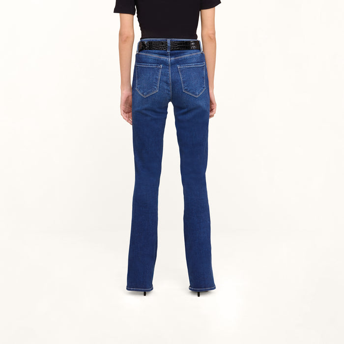 A person stands facing away, wearing Petite Selma Bootcut Jeans in dark blue super stretch denim with a black belt and a short-sleeve black top, against a light background.