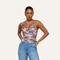 A woman wearing the Rasha Shirred Mesh Tank, featuring a pink floral pattern and square neckline, pairs it with blue jeans as she stands facing forward with her hands in her pockets against a plain light background.