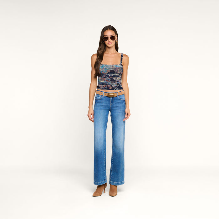 Woman wearing sunglasses, a Rasha Shirred Mesh Tank, blue flared jeans with a tan belt, and brown heeled shoes stands against a plain white background.
