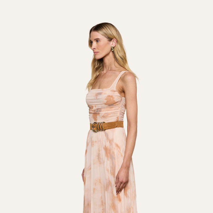 Woman in the Rasha Shirred Mesh Tank, a sleeveless peach and cream abstract print top, styled with a wide brown belt. She stands sideways against a plain light background, wearing small hoop earrings and her long blonde hair down.