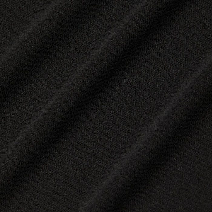 Close-up of the Raye Slip Lining Dress in black stretch jersey fabric, featuring diagonal, evenly spaced folds that create a soft and subtle textured pattern. The surface appears smooth and matte, with shadows accentuating the gentle contours of the dress’s pleats.