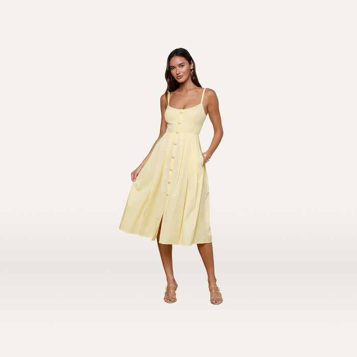 Wearing the Reanne Midi Dress, a woman stands against a plain white background. The light yellow sleeveless dress features thin straps, convenient pockets, and a smocked back for added comfort.