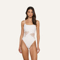 A woman models the Remi One-Piece Swimsuit, featuring thin straps, butterfly appliqué, and decorative side cutouts, set against a plain light background.