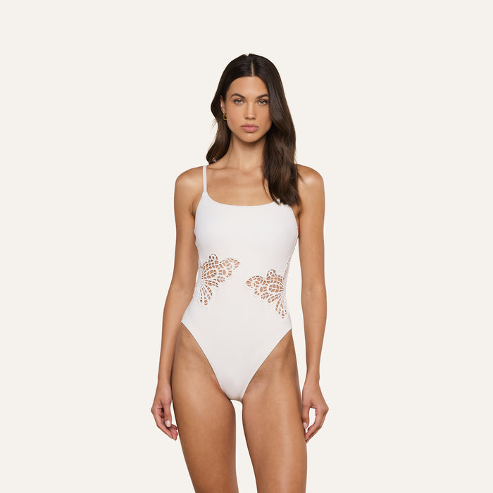 A woman models the Remi One-Piece Swimsuit, featuring thin straps, butterfly appliqué, and decorative side cutouts, set against a plain light background.