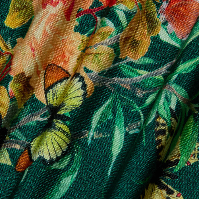 A close-up of the Remi One-Piece Swimsuit, showcasing green fabric adorned with a vibrant floral-butterfly print featuring yellow and orange flowers, lush green leaves, and a pale yellow butterfly with striking black accents.