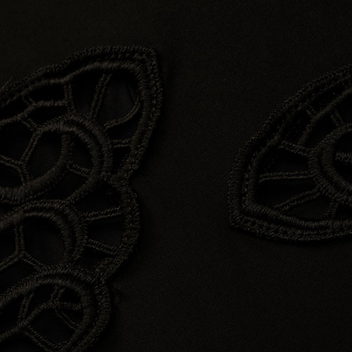 Close-up of the Remi One-Piece Swimsuit’s black fabric, featuring geometric, lace-like embroidered patterns reminiscent of poolside glamour. The textured embroidery creates a subtle contrast against the smooth background.